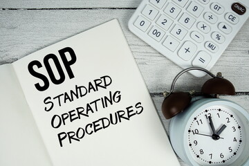 SOP Standard Operating Procedures text on paper notebook page with alarm clock and calculator on...