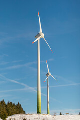 Fototapeta premium Wind turbines on a snowy mountain plateau in Neklid, Czech Republic – modern renewable energy technology contrasted with a rusty old windmill and clear winter skies