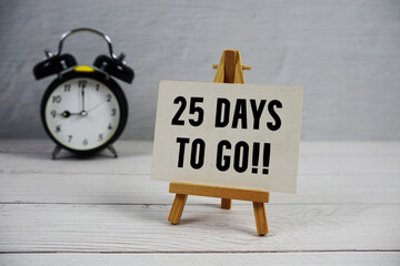 25 Days To Go! text with easel and alarm clock on wooden background