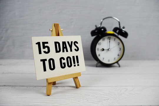 15 Days To Go! text with easel and alarm clock on wooden background