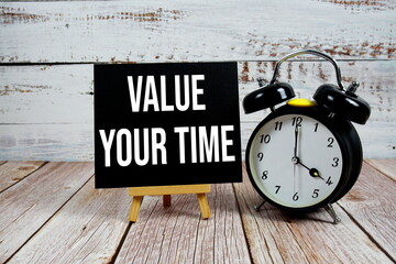 Value Your Time text with easel and alarm clock on wooden background