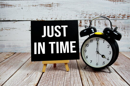 Just In Time text with easel and alarm clock on wooden background