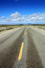 Desert highway in California U.S.A. with mountains on the horizon, blue sky and clouds, symbolic of a  journey looking towards a bright future