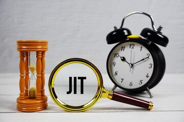 JIT abbreviation of Just In Time text with alarm clock on wooden background