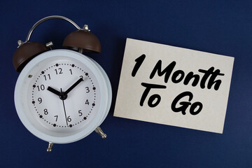 1 Month To Go text written on paper with alarm clock on blue background