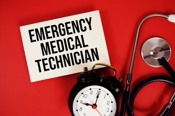Emergency Medical Technician text written on paper card with stethoscope and alarm clock on red background