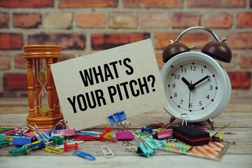 What's Your Pitch? text on paper card with alarm clock and stationary on wooden background