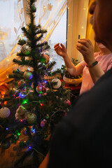 Joyful couple places colorful ornaments on their Christmas tree, surrounded by festive lights in a warmly decorated