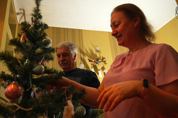 Couple shares joyful moments indoors as they decorate a Christmas tree with colorful ornaments and lights