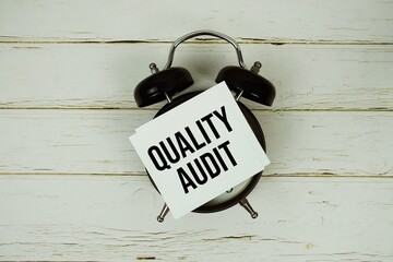 Quality Audit text message on paper with alarm clock on wooden background