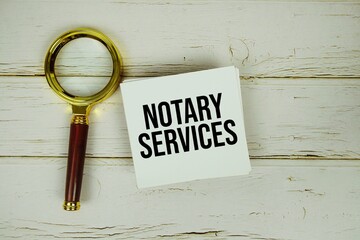 Notary Services text message on paper with magnifying glass on wooden background
