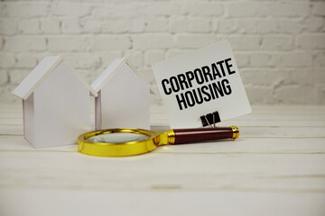 Corporate Housing text message on paper with magnifying glass and house model on wooden background
