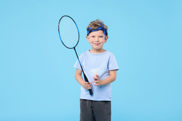 Little boy with badminton racket and shuttlecock on light blue background