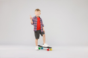 Little boy with penny board showing V-sign on gray background