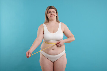 Weight loss. Plus size woman measuring waist with tape on light blue background