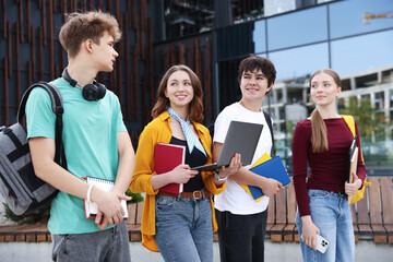 Teenagers with laptop and books near building outdoors