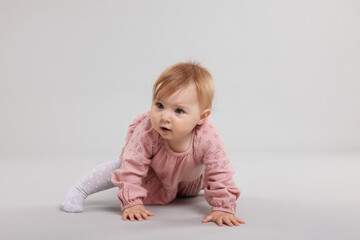 Cute little baby crawling on light grey background