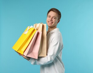 Cheerful man with shopping bags on light blue background