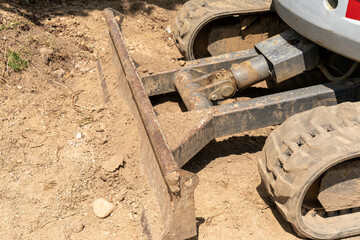Dozer end of small excavator with rubber chains, used to flatten and level the ground.