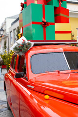 A red vintage car with colorful Christmas gifts on the roof. New Year's holiday background, holiday spirit.