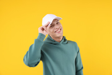 Young man wearing stylish white baseball hat on yellow background