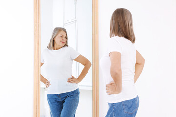Beautiful senior woman looking at herself in mirror indoors