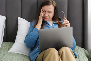 Woman with vision problem using laptop on bed at home