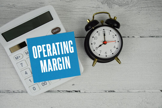 Operating Margin text with calculator and alarm clock  on wooden background