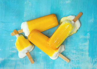 4 melting popsicles ice cream with  wooden sticks showing vibrant yellow color on a blue background...