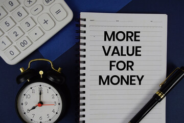 More Value for Money text written on notepad with calculator and alarm clock on navy blue background