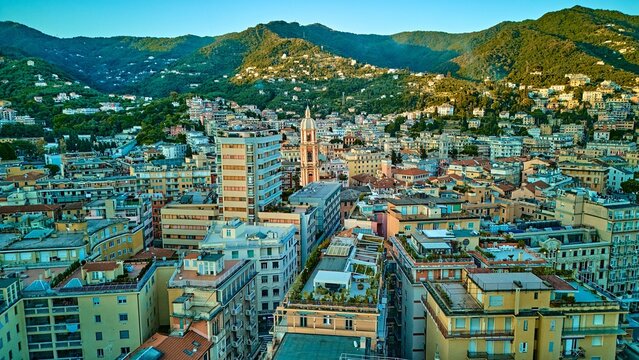 Wide aerial skyline of Rapallo city nestled between emerald Ligurian mountains and Mediterranean coast with basilica campanile as focal point, Italian Riviera, Italy. Sunset drone view