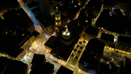 Overhead night aerial of Rapallo Basilica of Saints Gervasius and Protasius with glowing bell-tower in the old town, Italian Riviera, Liguria, Italy. Night drone view