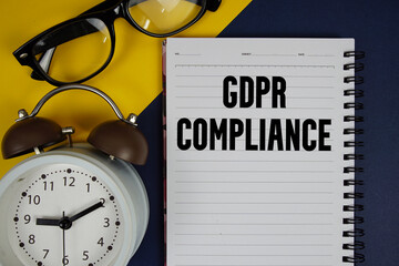 GDPR Compliance text written on notepad with alarm clock on blue background