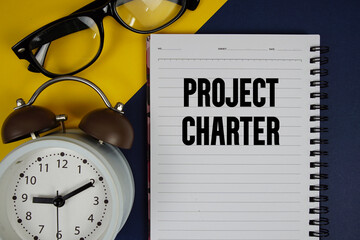 Project Charter text written on notepad with alarm clock on blue background