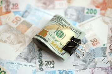 Bunch of US dollar bills lies on big amount of Brazilian reais banknotes close up
