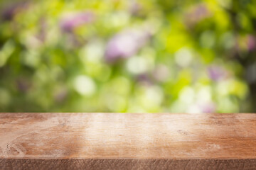 A clean wooden tabletop with soft natural texture stands against a vibrant, blurred floral garden background, perfect for spring or summer product presentations