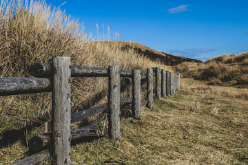 Obraz premium Wooden Fence in Dry Grass Field with Blue Sky at Mount Aso, Kyushu, Japan