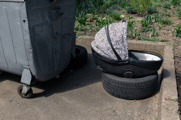Discarded baby carriage. Baby stroller next to a trash container
