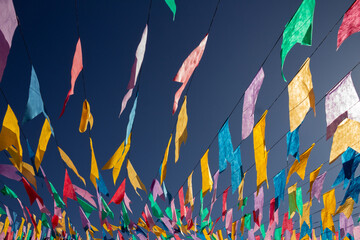 Close up em vários varais com bandeirolas coloridas balançando, penduradas em barbante, com céu azul ao fundo.
