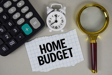 Home budget text with alarm clock, magnifying glass anc calculator on gray background