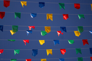 Céu azul com bandeirinhas coloridas penduradas em barbante, balançando com o vento. Festa junina.