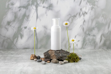 a container for skin care products on a podium made of stone and moss and daisy flowers on a gray...