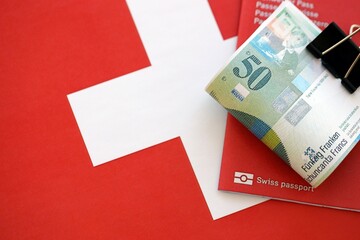 Swiss franc banknotes and passport on flag. The current francs money bills lies on flag with pass