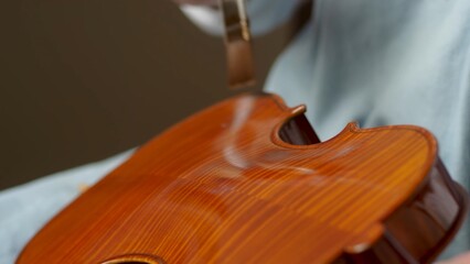 Skilled craftsman applying glossy varnish to handmade violin, revealing rich wood texture and precision within traditional workshop setting