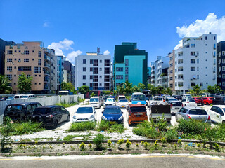 An outdoor parking lot filled with various cars, set against multi-story buildings. Represents...