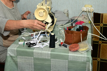 The picture shows a seamstress at work. The seamstress is making a seam on the fabric using a sewing machine.