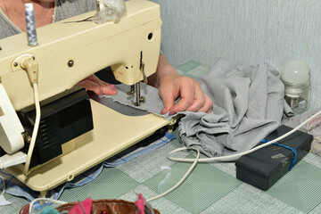 The picture shows a seamstress at work. The seamstress is making a seam on the fabric using a...