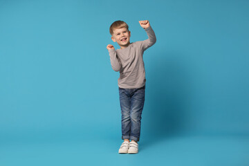 Happy little boy dancing on light blue background