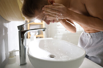 Man washing his face over sink in bathroom