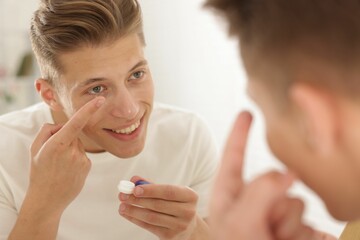 Man putting in contact lens near mirror at home